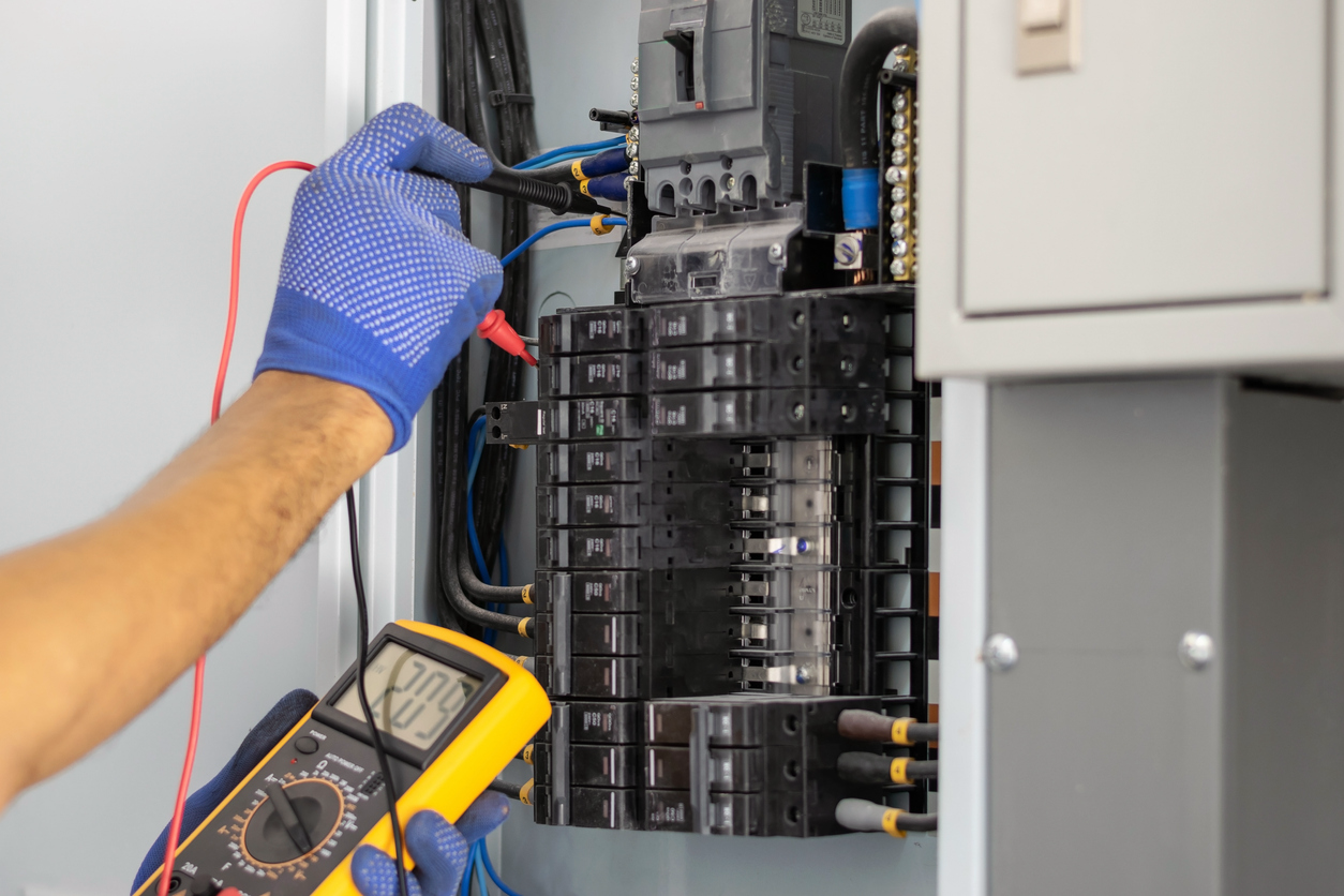 The gloved hands of an electrician checking an electrical panel.